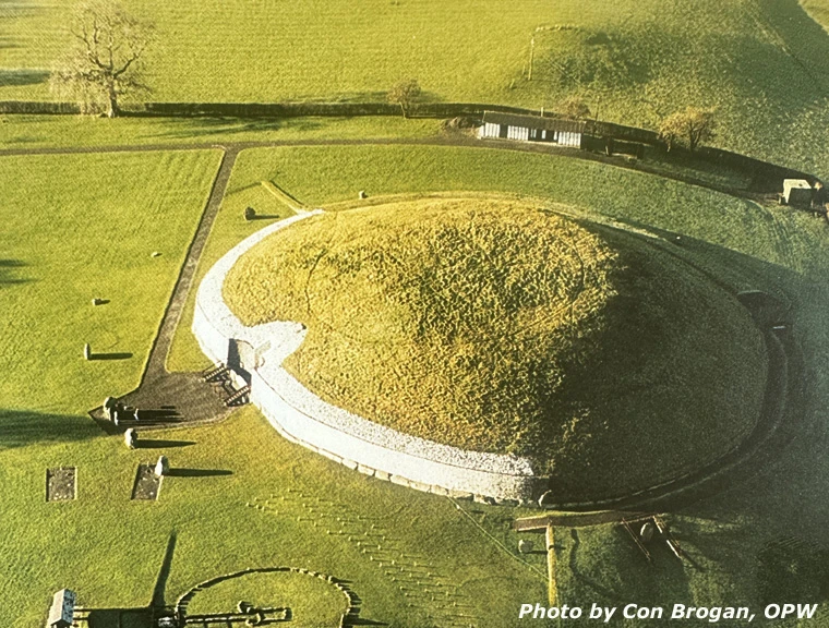 Early morning aerial view of Newgrange mound, quartz facade, entrance and standing stones in green fields.
